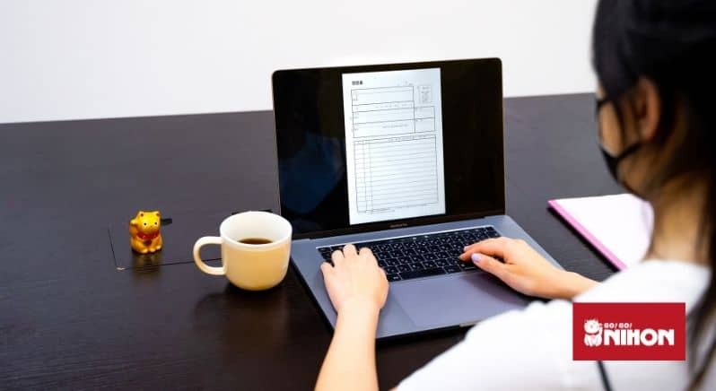 en lyckokatt, kopp kaffe och en dator - en person syns bakifrån fylla i ett CV på datorn inför en framtida japan-relaterad karriär