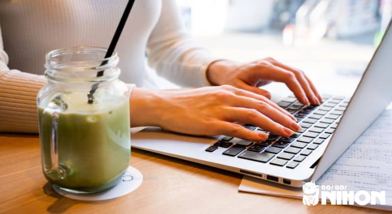 Person searching on a laptop about the digital nomad visa in Japan while an iced matcha latte sits on the table next to them.