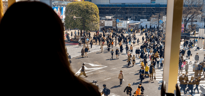 Eine Frau überblickt Menschen, die von oben über den Shibuya Crossing gehen.