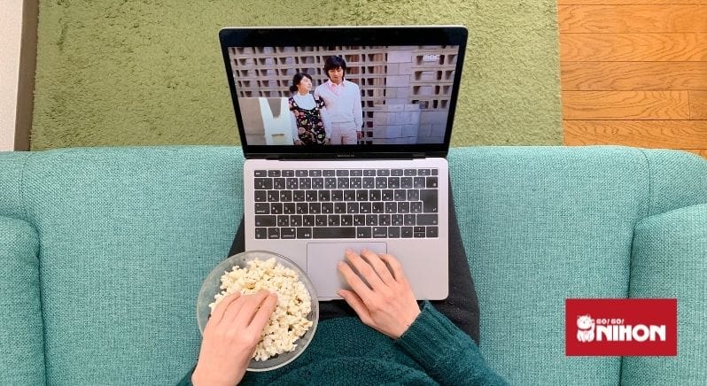 Imagen de una persona viendo un programa japonés en una computadora portátil mientras come palomitas de maíz
