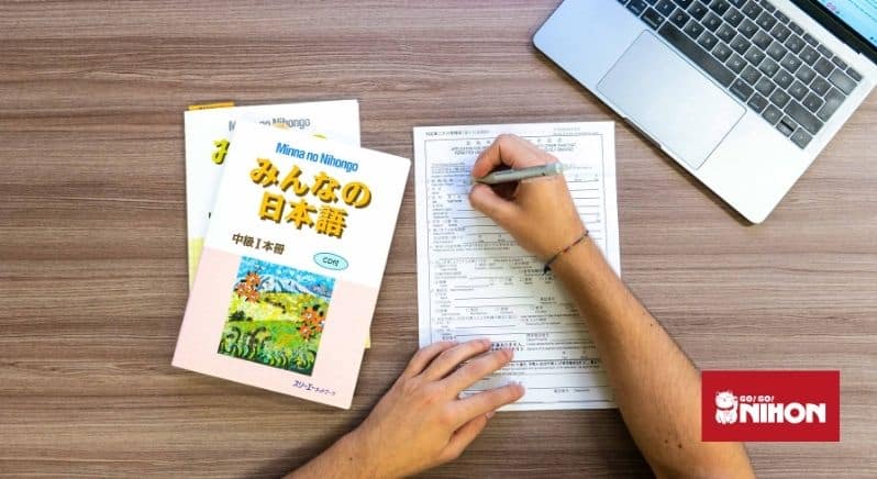 flat lay image of person filling in a form by hand, with Japanese language text books and a laptop on the side