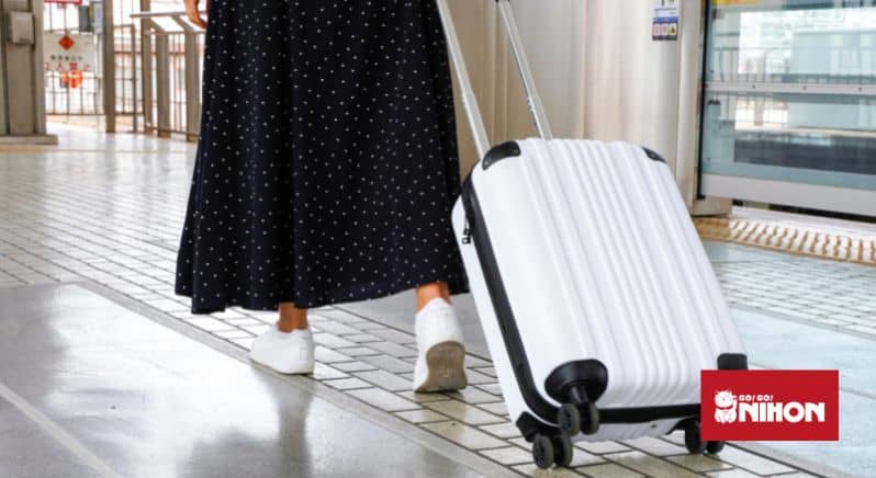En kvinna som rullar en vit resväska bakom sig på en tågperrong