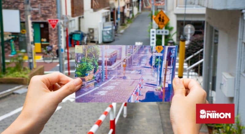 Image of person holding an image from Japanese animated movie Your Name up against the real-life location in Yotsuya, Tokyo