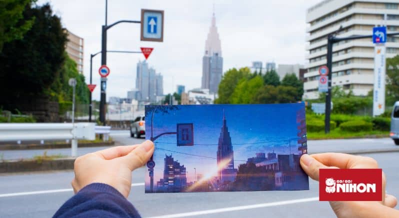 Imagen de una persona sosteniendo una imagen del edificio NTT Docomo Yoyogi con el edificio de la vida real como telón de fondo