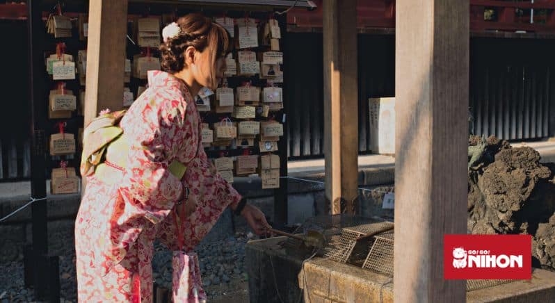 Kvinna iklädd i en rosa kimono som renar sina händer vid en Shinto-helgedom