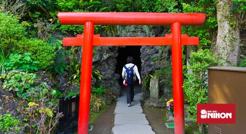 Image of a person walking with a red torii gate in the forefront