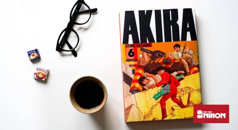Japanese manga book, glasses, a cup of coffee, and two pieces of Japanese candy displayed on a white background.