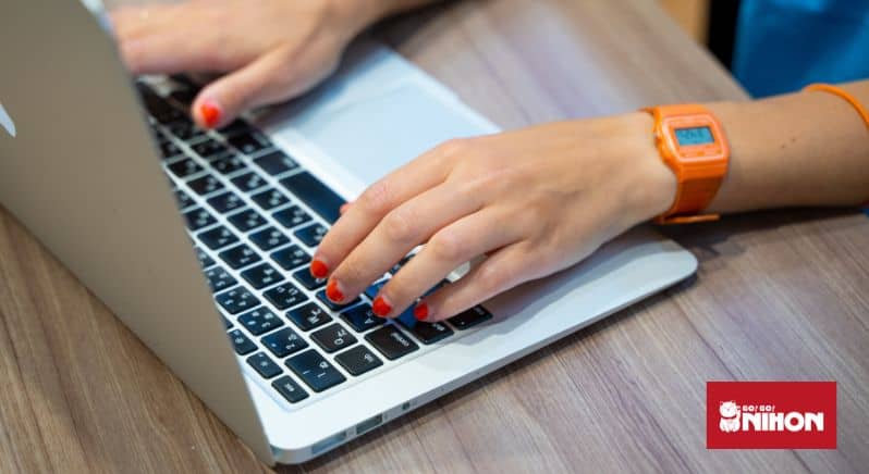 Someone wearing a digital orange wristwatch, typing on a keyboard.
