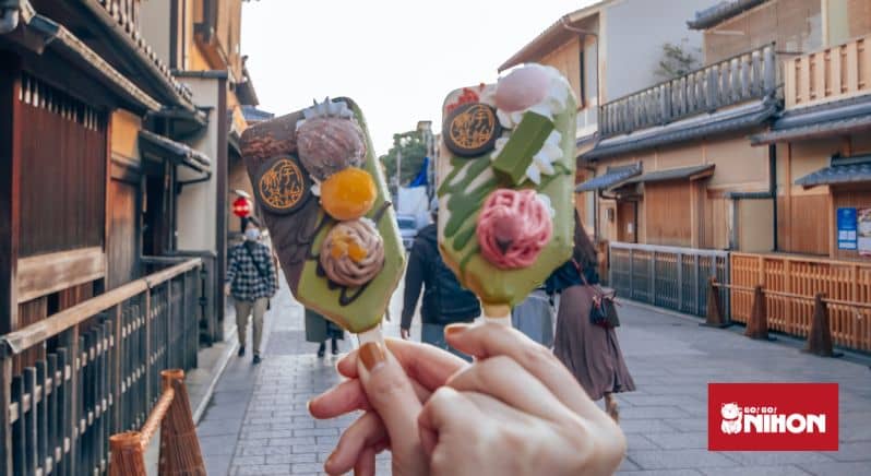 Två matcha-glassar hålls upp framför en gata med traditionella hus i Kyoto i Japan.