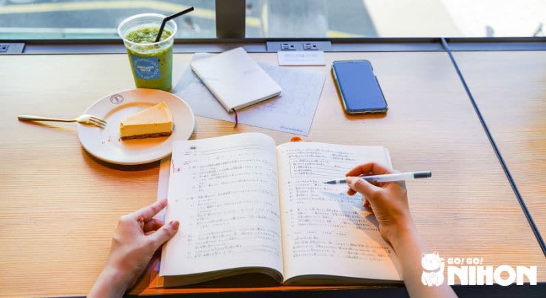 Pessoa estudando japonês em um café. Um matcha gelado e um cheesecake estão sobre a mesa.