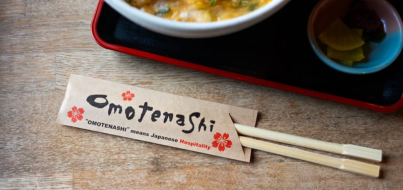 Ätpinnar som ligger platta på ett bord inuti ett omslag av papper med omotenashi-design.