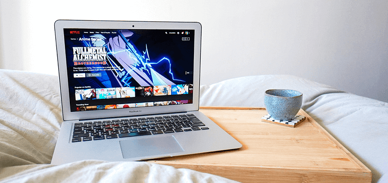 An open laptop displayed on a bed with anime shown on the screen.