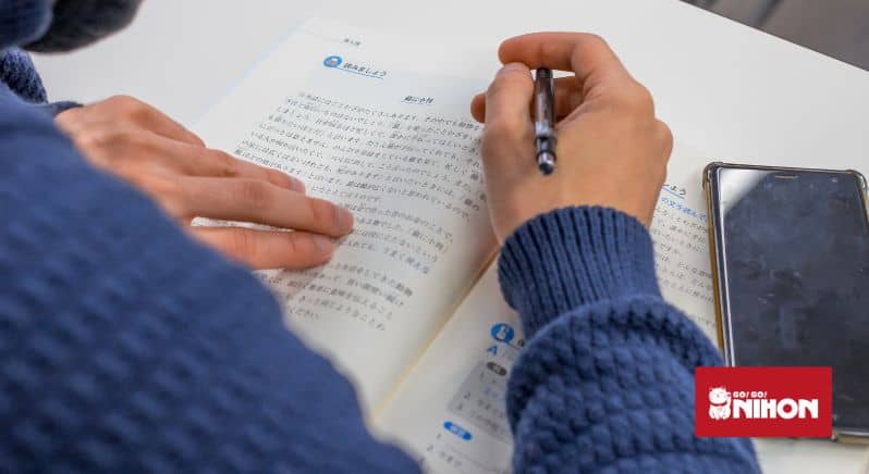 Image of person holding a pen and reading through a Japanese language textbook
