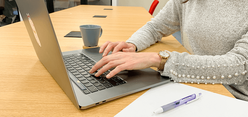 Person in a grey sweater typing on a laptop.