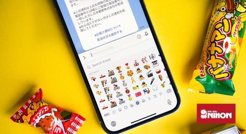 Mobile phone on yellow backdrop with text message on screen in Japanese, with Japanese snacks nearby